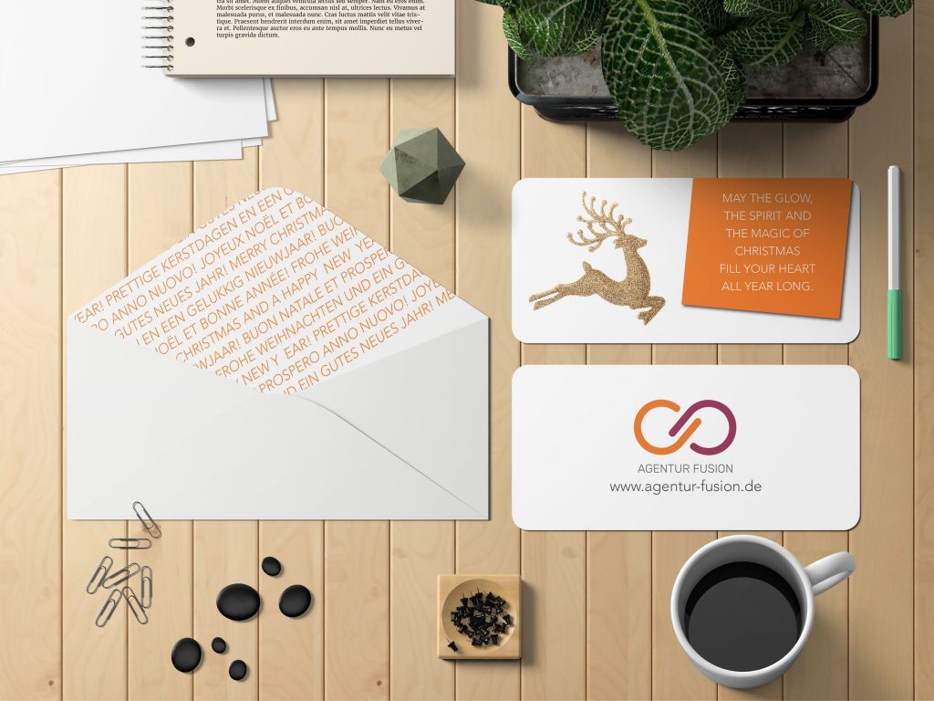 Weihnachtskarte Agentur Fusion mit goldenem Rentier, Grußfeld und Umschlag mit mehrsprachigem Futter; Logo-Karte in CI auf Holzuntergrund